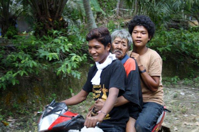 Ein alter Mann, der nicht mehr laufen kann, wird von zwei jungen Orang Rimba mit dem Motorrad weggefahren.