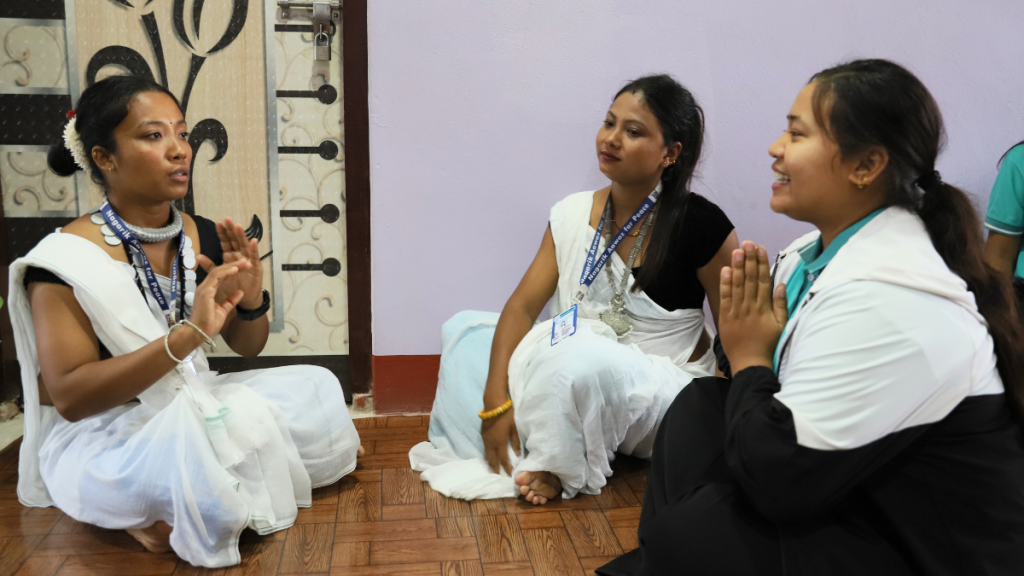 Drei junge Frauen mit Schwarzen Kleidern und weißen Umhängen sitzen auf dem Boden. © Ganga Sagar Rai